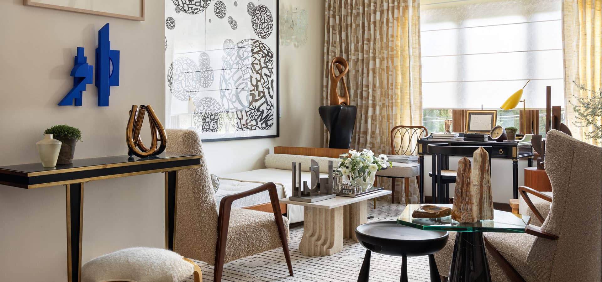 Pirela Atelier. Eclectic drawing room featuring a daybed, high-back bouclé wing chair, and a mid-century desk nook by the window.