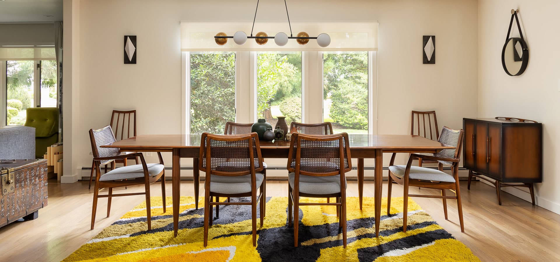 Pirela Atelier. Bright dining space featuring a linear modern chandelier and a vintage-style console cabinet.