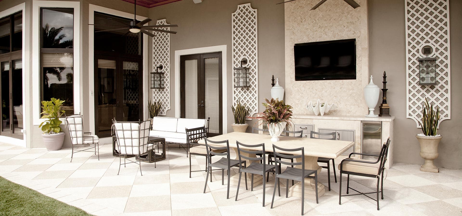 Pirela Atelier. Luxury covered patio with outdoor dining table, built-in TV, and ceiling fans, decorated with tall white trellises.