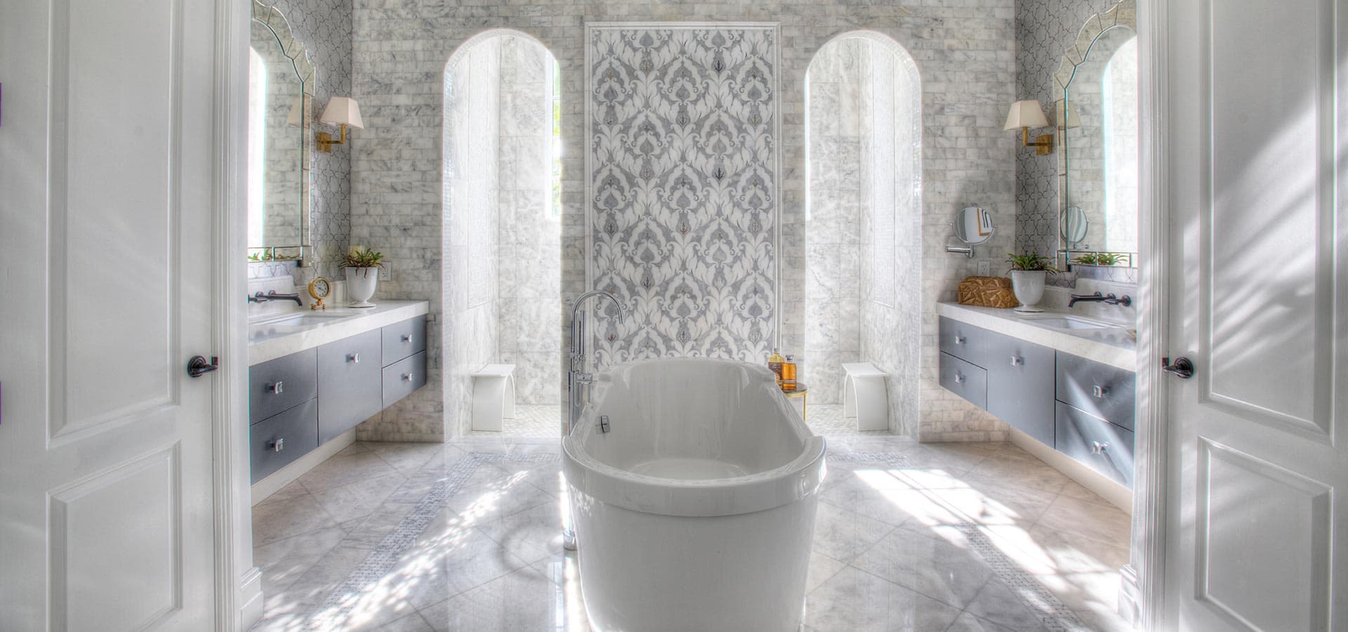 Pirela Atelier. Luxury symmetrical master bathroom featuring a freestanding tub, gray marble tile, and arched walk-in shower niches.